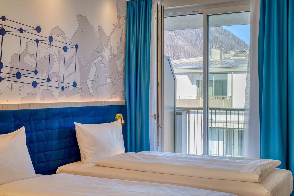A hotel room with a large bed, a headboard with a geometric design, and a view of a mountain through a sliding glass door.