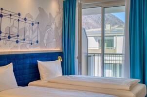 Habitación de hotel con una cama grande, cabecera con diseño geométrico y vista a una montaña a través de una puerta corrediza de vidrio.
