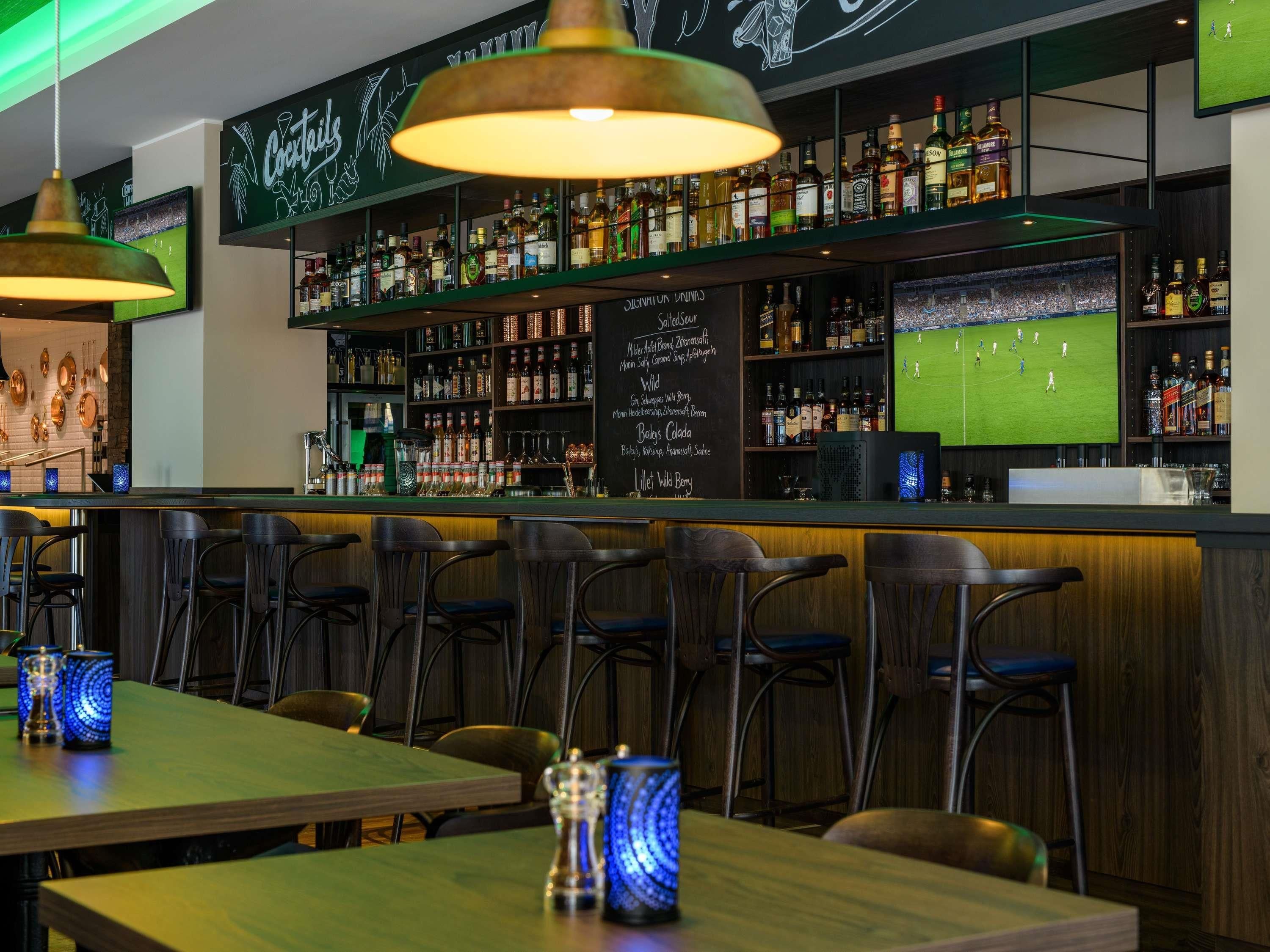 Una zona de bar con una variedad de botellas de licores, un menú en una pizarra y una pantalla de televisión mostrando un evento deportivo.