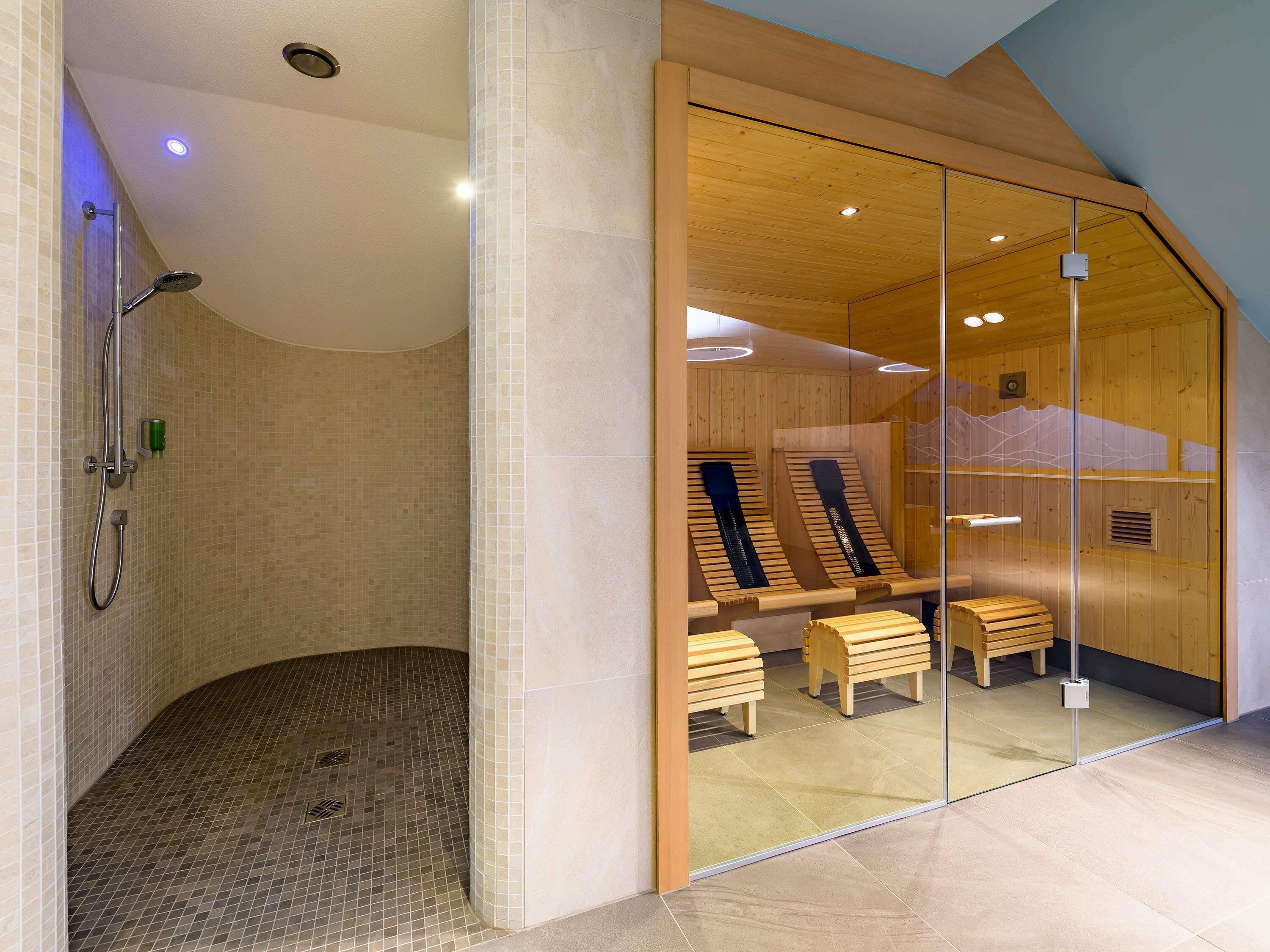 A modern bathroom with a shower, wooden benches, and a glass partition.