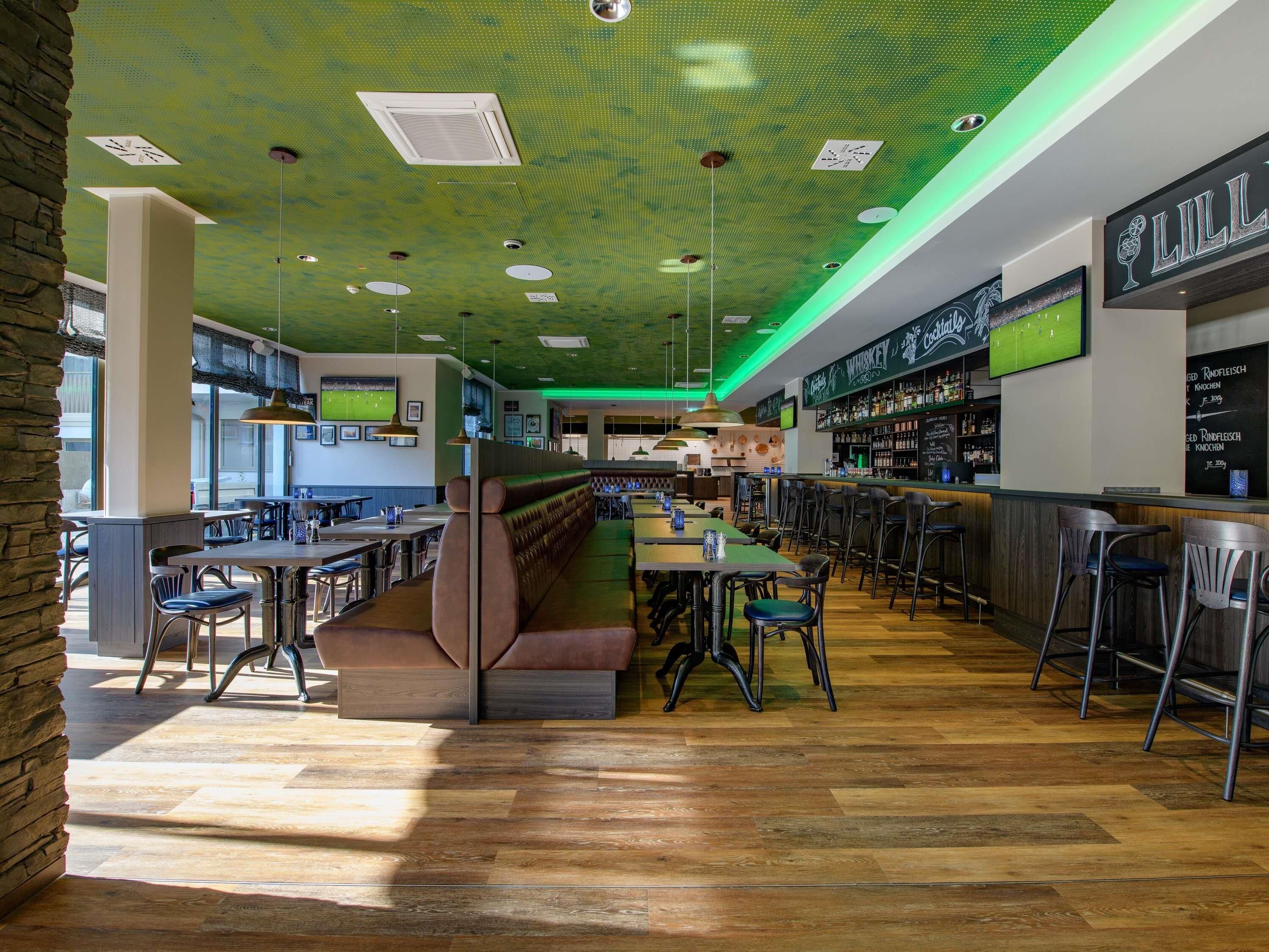 Een moderne bar met een groen plafond, houten vloer en een bargedeelte met krukken.