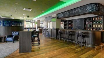 A modern bar area with a wooden floor, bar stools, and a variety of liquor bottles.