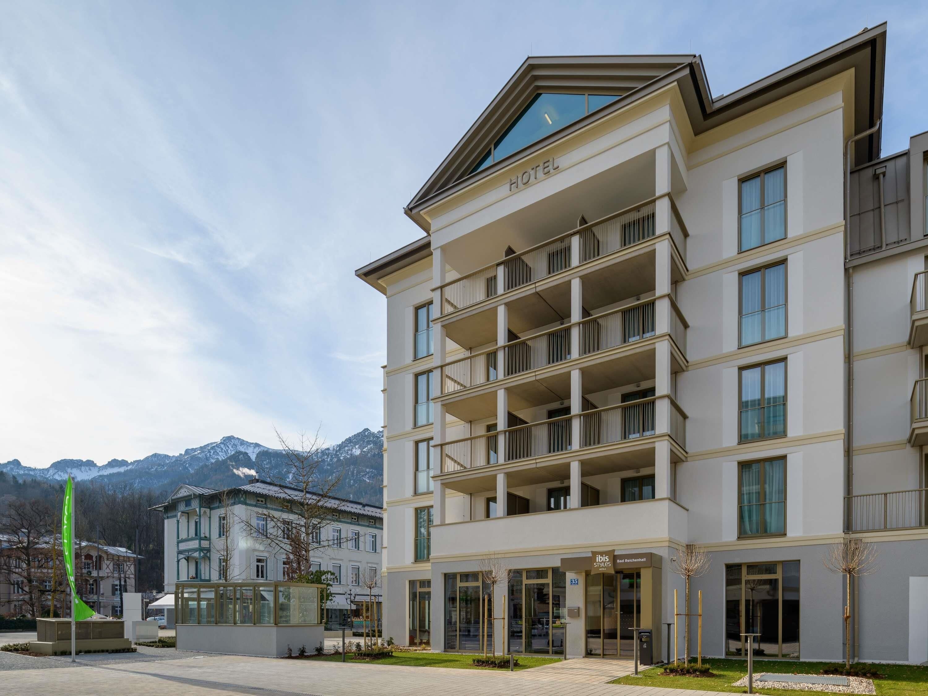Et hotel med flere altaner, en moderne facade og bjergudsigt i baggrunden.