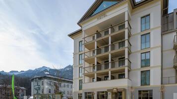 Et hotel med flere altaner, en moderne facade og bjergudsigt i baggrunden.
