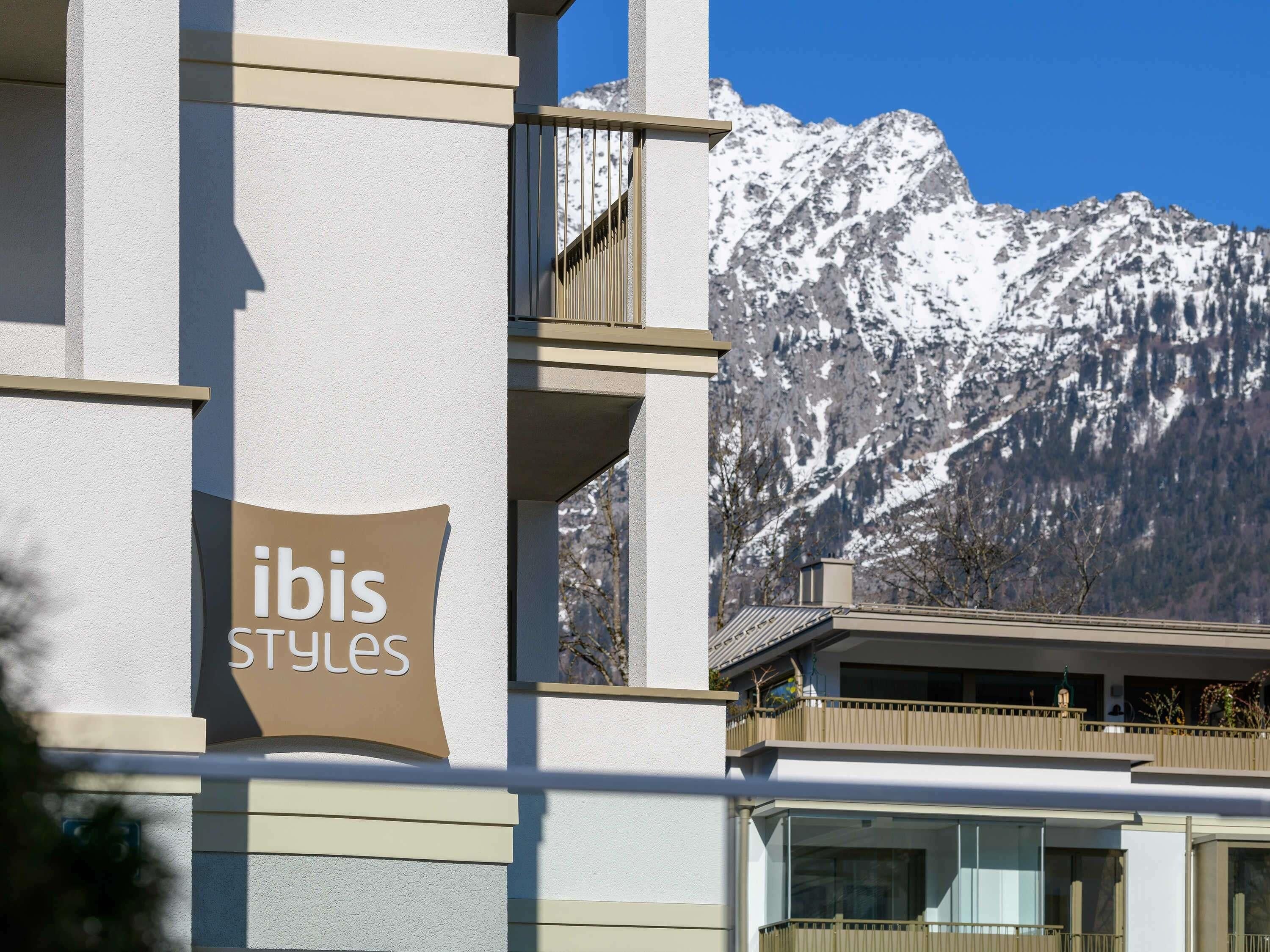 Un edificio con un letrero que dice 'ibis Styles' y montañas al fondo.
