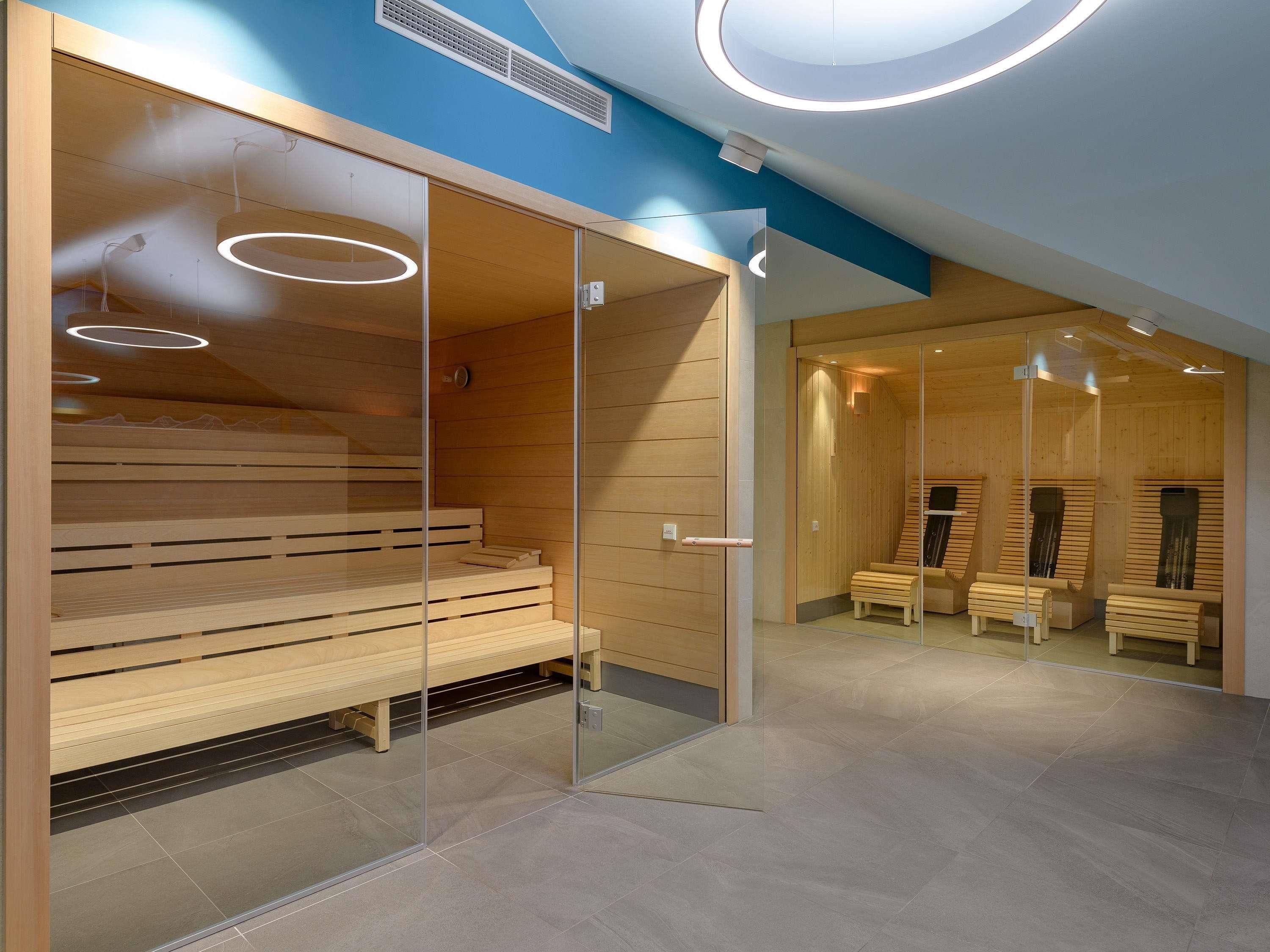 A modern sauna room with wooden benches, glass partitions, and circular ceiling lights.
