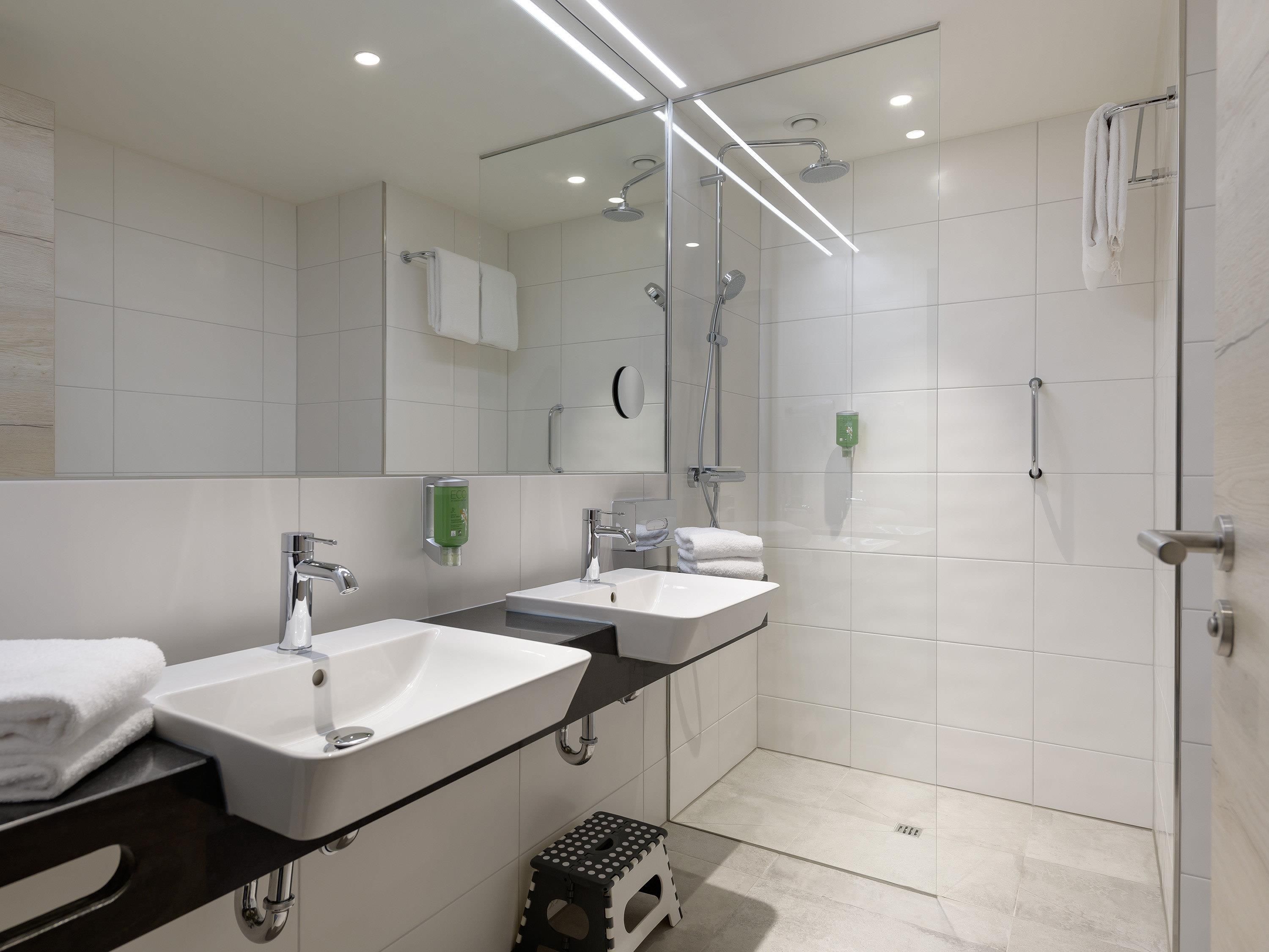Un baño moderno con dos lavamanos, una ducha y zona de ducha con mampara de vidrio.