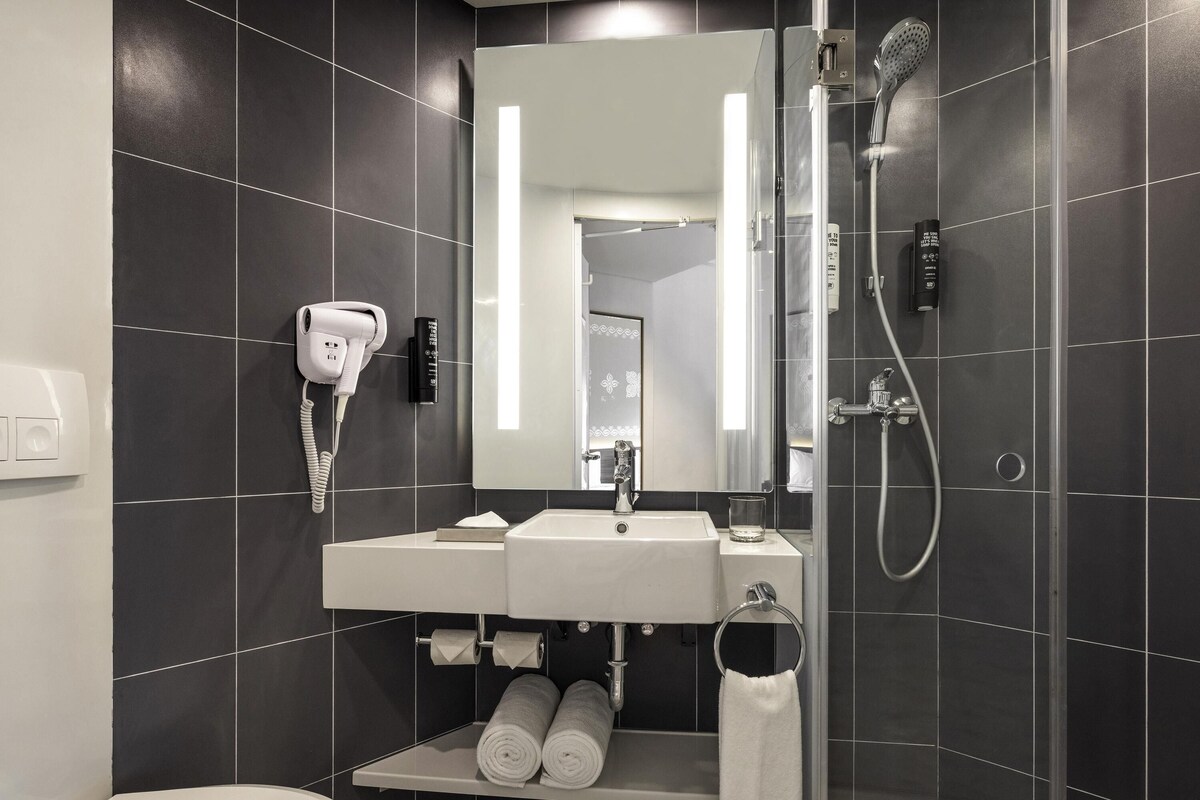 A modern bathroom with a white sink, a mirror, a hairdryer, and a shower.