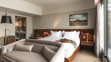 Una habitación de hotel con cama, sofá, escritorio, lámpara, espejo y un cuadro en la pared.