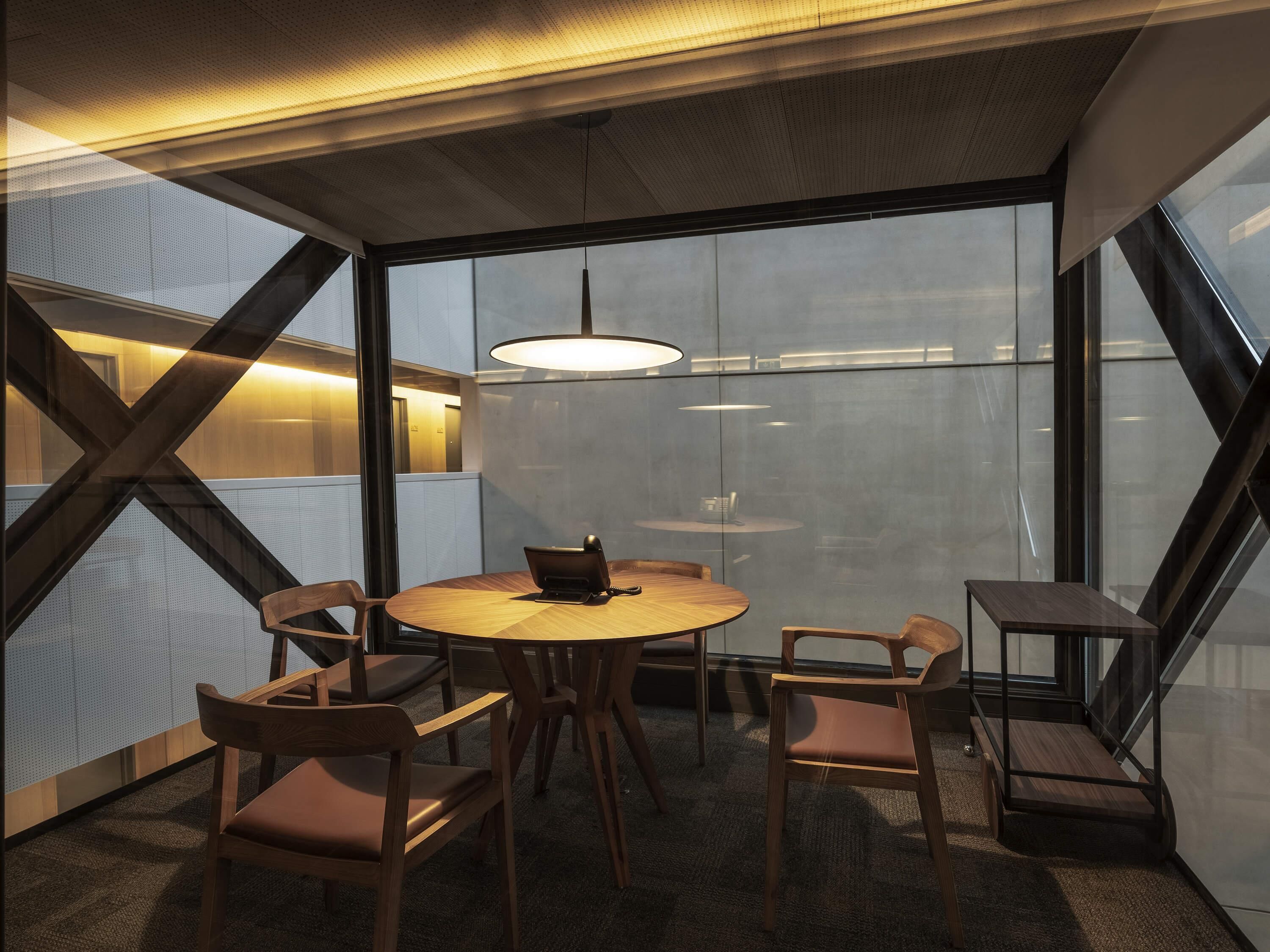A modern meeting room with a round table, chairs, a telephone, and a large window.