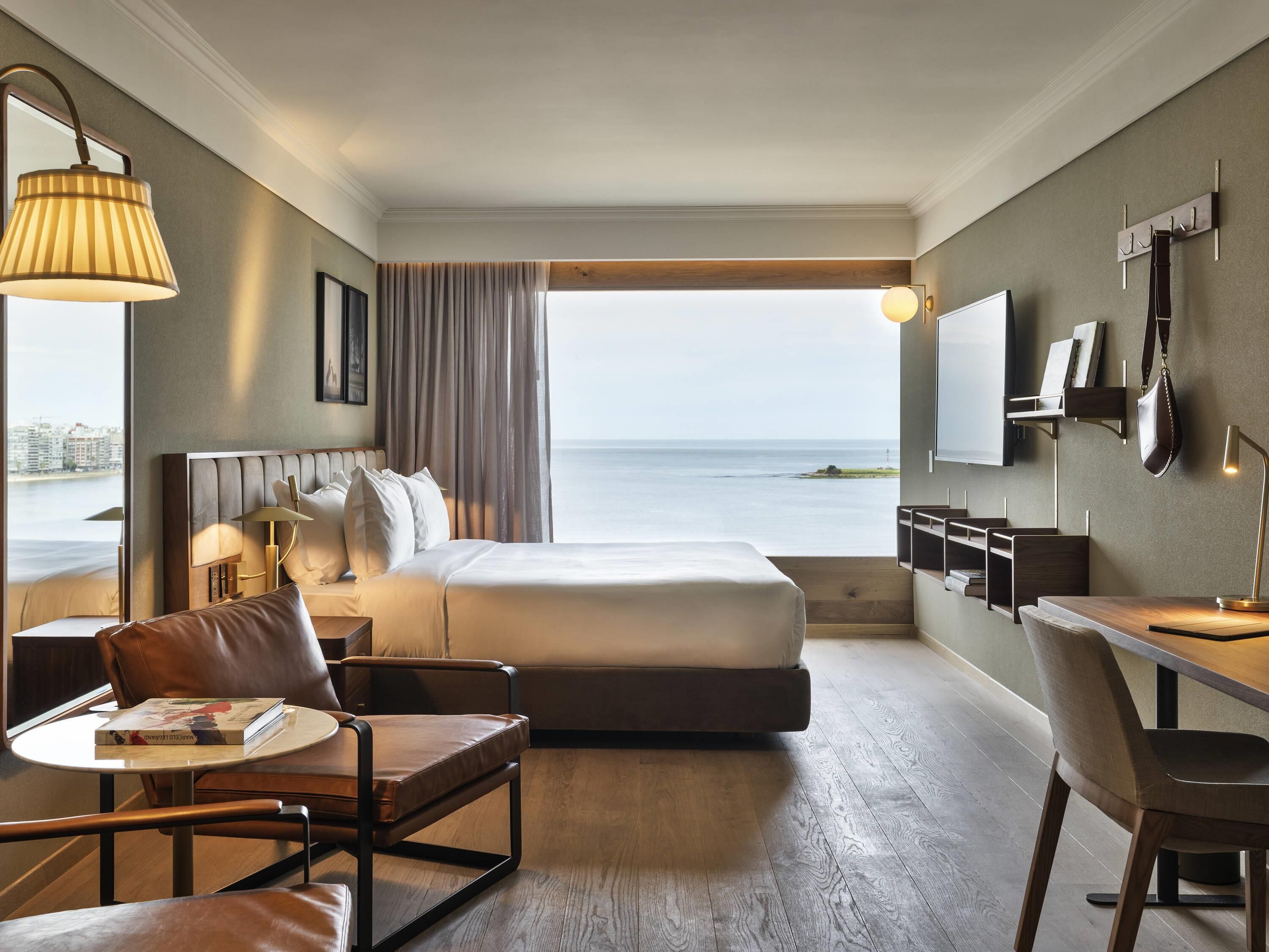 Ein Hotelzimmer mit Bett, Schreibtisch, Stuhl, Fernseher und Blick auf das Meer.