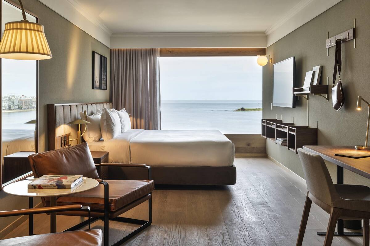Un cuarto de hotel con cama, escritorio, silla, televisor y vista al mar.