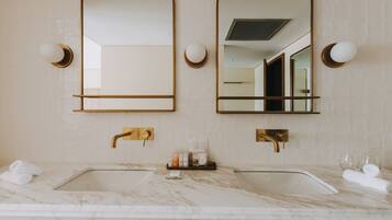 Ein Badezimmer mit zwei Waschbecken, Marmorplatten, goldenen Armaturen und Spiegeln an der Wand.