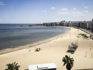 Ein Strand mit sandigem Ufer, einem Rettungsturm und einer Reihe von Gebäuden im Hintergrund.