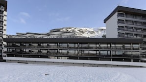 Ein modernes Gebäude mit mehreren Stockwerken und großen Fenstern, vor einer verschneiten Landschaft mit einem Berg im Hintergrund.