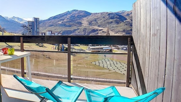 Ein Balkon mit Bergblick, ein Tisch mit einer roten Tasse und ein blauer Stuhl.