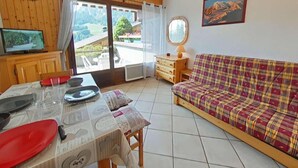 Ein gemütliches Wohnzimmer mit einem Holztisch, der zum Essen gedeckt ist, einer karierten Couch, einem Fernseher und einer schönen Aussicht durch die Glastür.