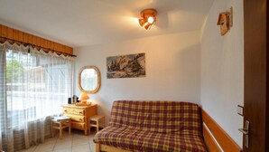 Ein gemütliches Zimmer mit einem Karo-Sofa, einem Holztisch mit Lampe, einem Fenster mit transparenten Vorhängen und einem Bild an der Wand.