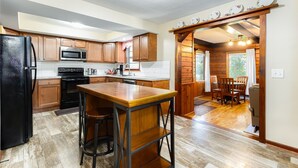 A modern kitchen with wooden cabinets, a stainless steel refrigerator, and a bar area with stools. - Home away from Home (South Bend)