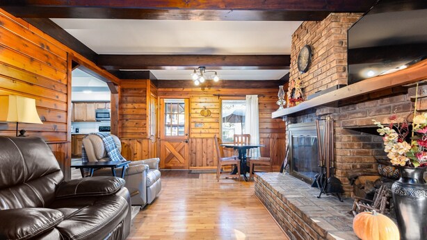 A cozy living room with a fireplace, leather sofa, wooden walls, and a dining area. - Home away from Home (South Bend)