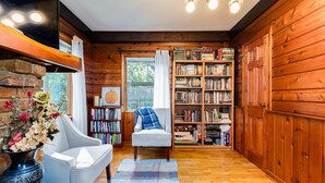 A cozy room with a fireplace, a bookshelf, a comfortable chair, and a large window. - Home away from Home (South Bend)