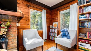 A cozy room with wooden walls, two white armchairs, a bookshelf, and a fireplace. - Home away from Home (South Bend)