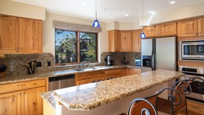 A modern kitchen with granite countertops, wooden cabinets, stainless steel appliances, and a large island. - The Pines 202 2 Bedroom Condo by RedAwning (Steamboat Springs)