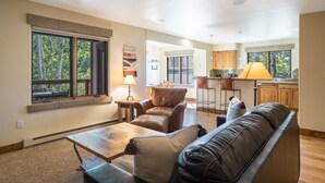 A spacious living room with a leather sofa, a coffee table, and a dining area with a lamp. - The Pines 202 2 Bedroom Condo by RedAwning (Steamboat Springs)