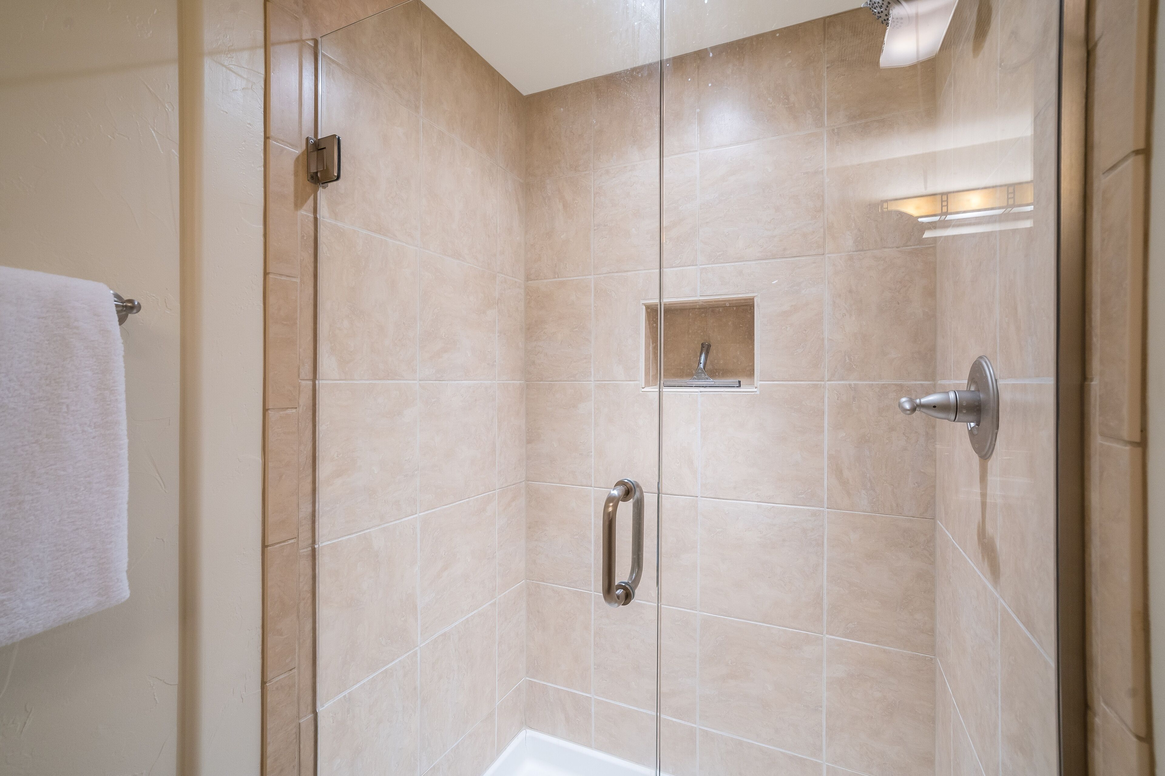 Un baño moderno con baldosas color crema, cabina de ducha de vidrio, bañera blanca y toallero.