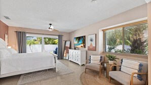 A bedroom with a bed, a dresser, a chair, a television, and a window with blinds. - Coccoloba 3 Bedroom Home by RedAwning (Holmes Beach)
