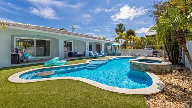 A swimming pool with a hot tub, surrounded by a white fence, and a grassy area with lounge chairs. - Coccoloba 3 Bedroom Home by RedAwning (Holmes Beach)