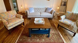 A living room with a tufted sofa, patterned armchairs, a wooden coffee table, and a decorative mirror.