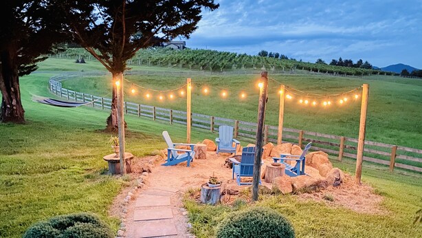 A rustic outdoor seating area with Adirondack chairs, a stone pathway, and string lights.