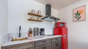 A kitchen with a marble countertop, a stainless steel sink, a red refrigerator, and a black range hood. - @ Marbella Lane - Rainbow House | Glampers Paradise (Joshua Tree)
