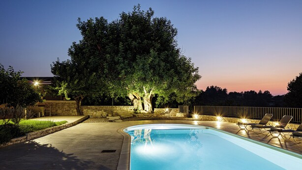 A swimming pool with a curved edge, surrounded by a stone wall and a wooden deck. - Mithonies Villa, with Private Pool & BBQ, Walking distance to shops (Rethymno)