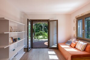 A modern room with a sliding glass door leading to a garden, a sofa with cushions, and built-in shelves.