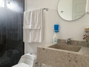 Casa de banho com toalha branca pendurada numa barra, lavatório com bancada de mármore, espelho e zona de duche.