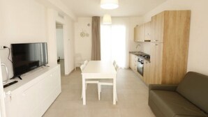 Um espaço compacto com mesa de jantar, sofá, televisão e pequeno espaço de cozinha.