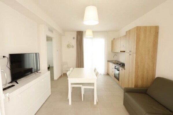 Un espacio habitable compacto con una mesa de comedor, un sofá, un televisor y una kitchenette.