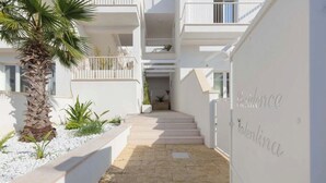 Um edifício moderno com fachada branca, uma palmeira e uma escadaria que leva a um andar superior.