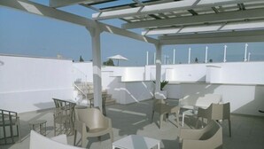 Terraço no telhado com mobiliário branco, incluindo cadeiras e mesas, e uma estrutura de pérgula.