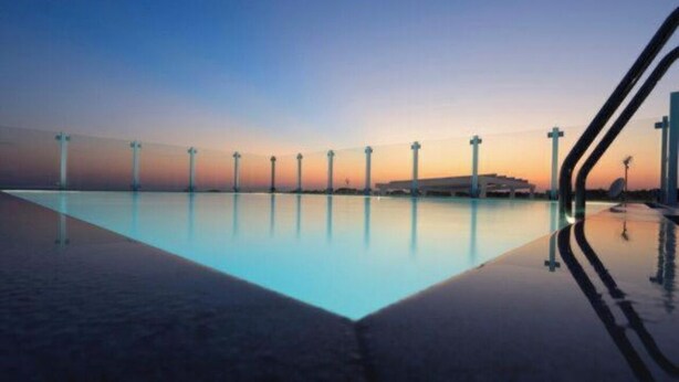 Piscina com vista para o pôr do sol, cercada por estruturas altas e céu claro.