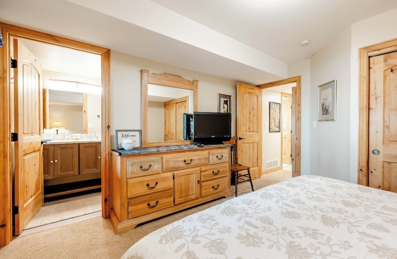 A bedroom with a large bed, wooden dresser, and a television.