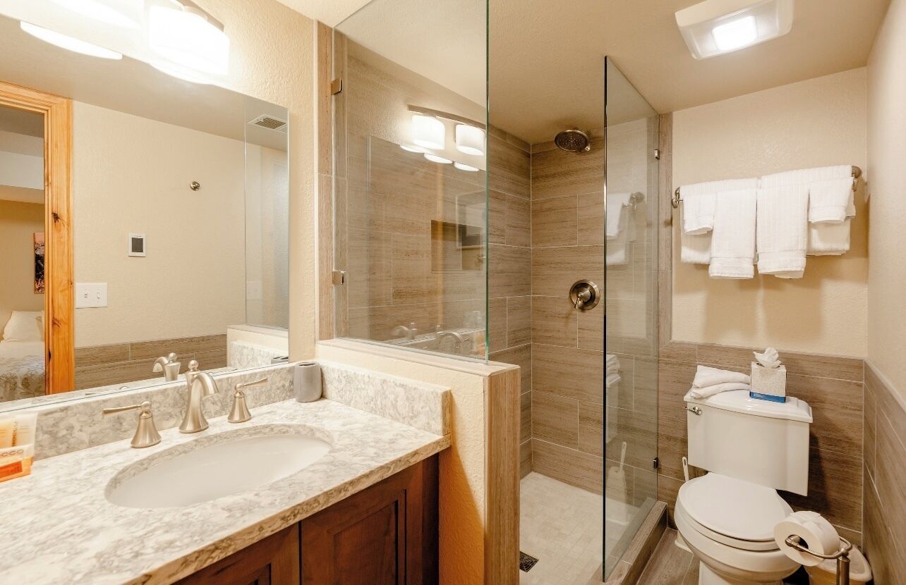 A modern bathroom with a glass-enclosed shower, a marble sink, and a toilet with a towel rack.