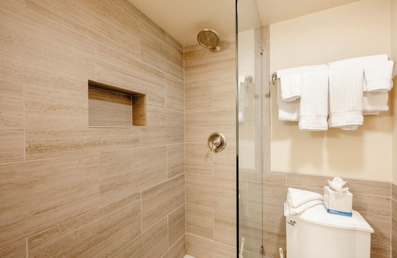 Un baño moderno con cabina de ducha de vidrio, un inodoro con caja de pañuelos y un perchero con varias toallas.