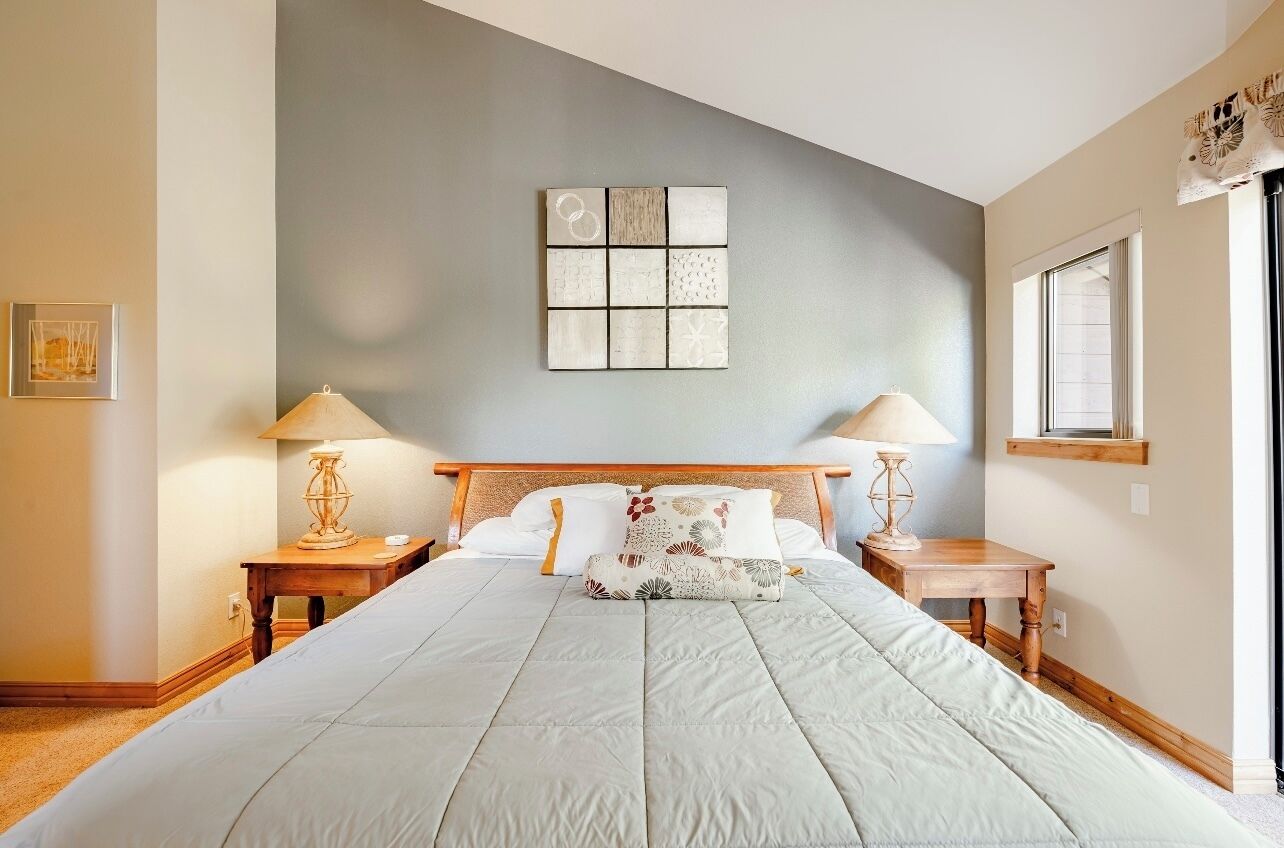 Un dormitorio con una cama grande, dos mesitas de noche con lámparas, una obra de arte en la pared y una ventana.