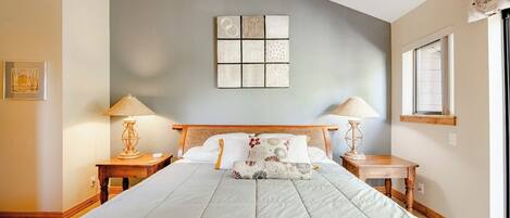 Un dormitorio con una cama grande, dos mesitas de noche con lámparas, una obra de arte en la pared y una ventana.