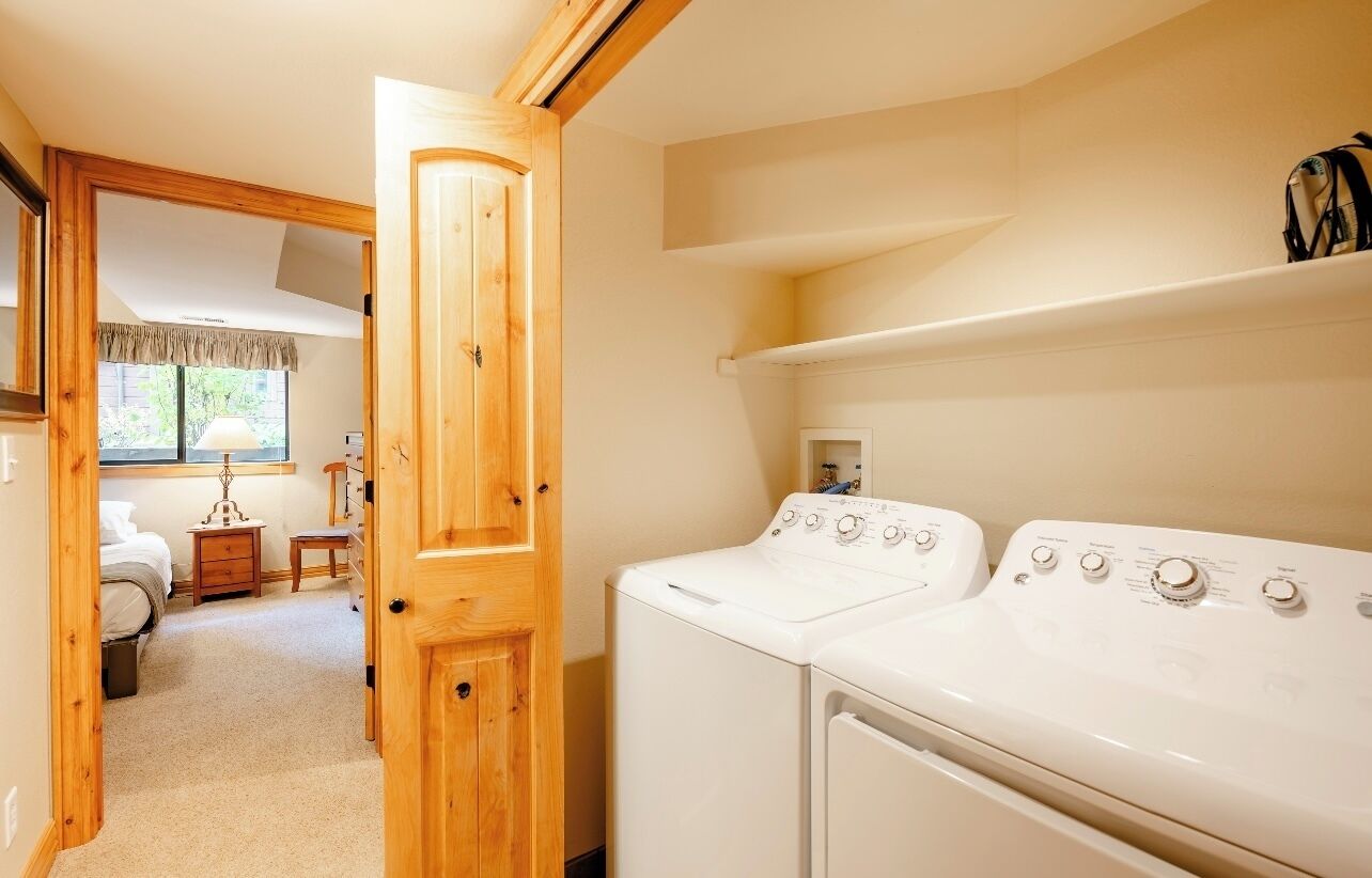 A laundry room with two white washing machines, a wooden door, and a window with a view of the outside.