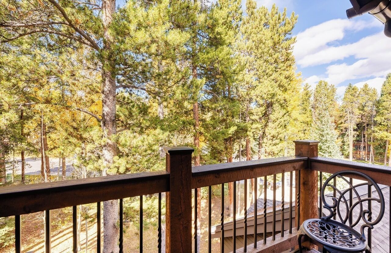 Una terraza de madera con baranda de metal, con vista a un bosque de altos pinos.