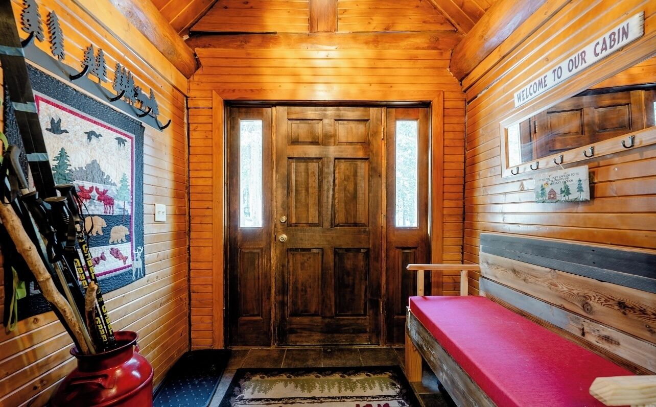 A wooden cabin interior with a wooden door, a welcome sign, a bench, and a wall-mounted rack.